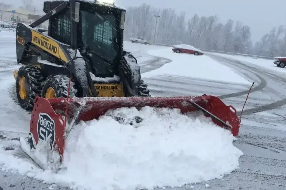 Skid steer with a plow pushing snow in a commercial parking lot